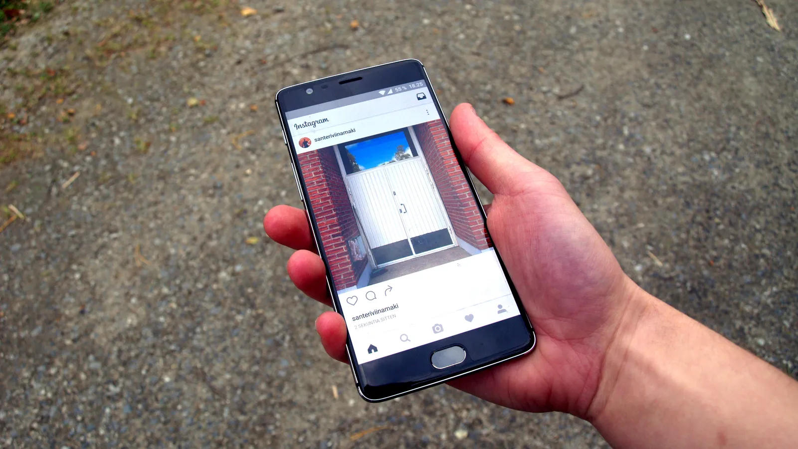 Mano sosteniendo un teléfono con la aplicación de Instagram abierta sobre un fondo de asfalto